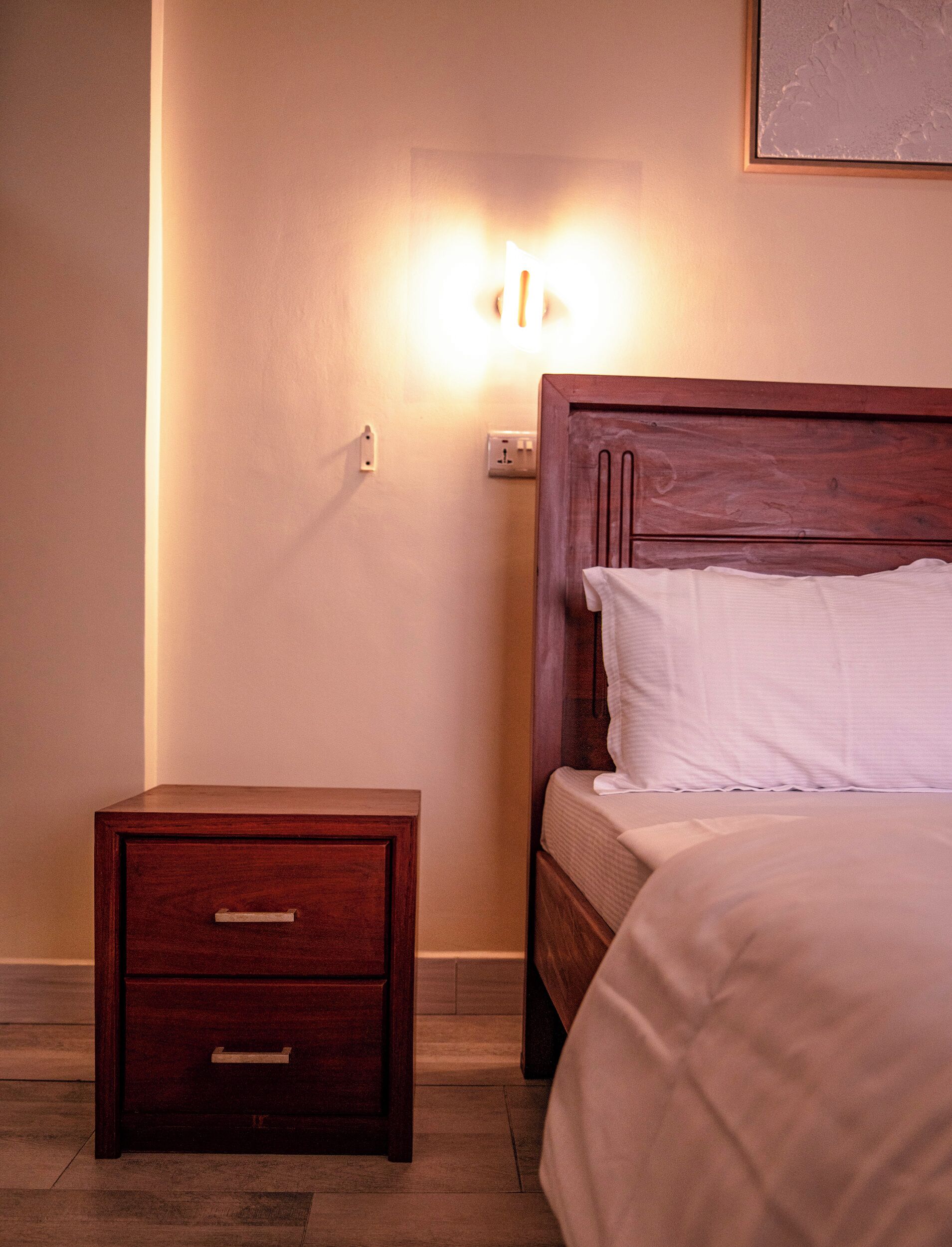 A neatly made bed with a wooden headboard and a nightstand with drawers.