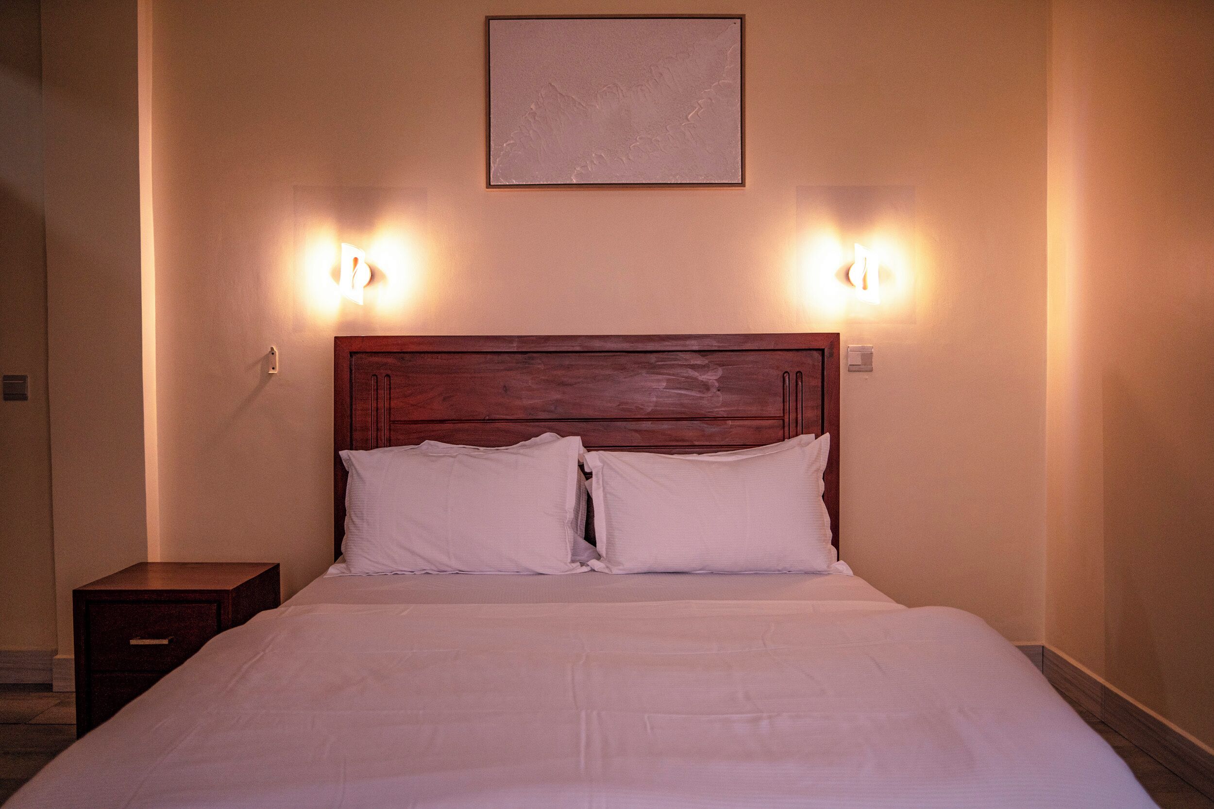 Una cama bien hecha con cabecera de madera y dos lámparas de noche.