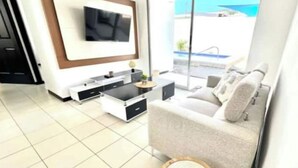 A modern living room with a sofa, a coffee table, a flat-screen TV mounted on the wall, and a view of the outdoors. - Welcome to your tropical getaway! 6 people (Herradura)