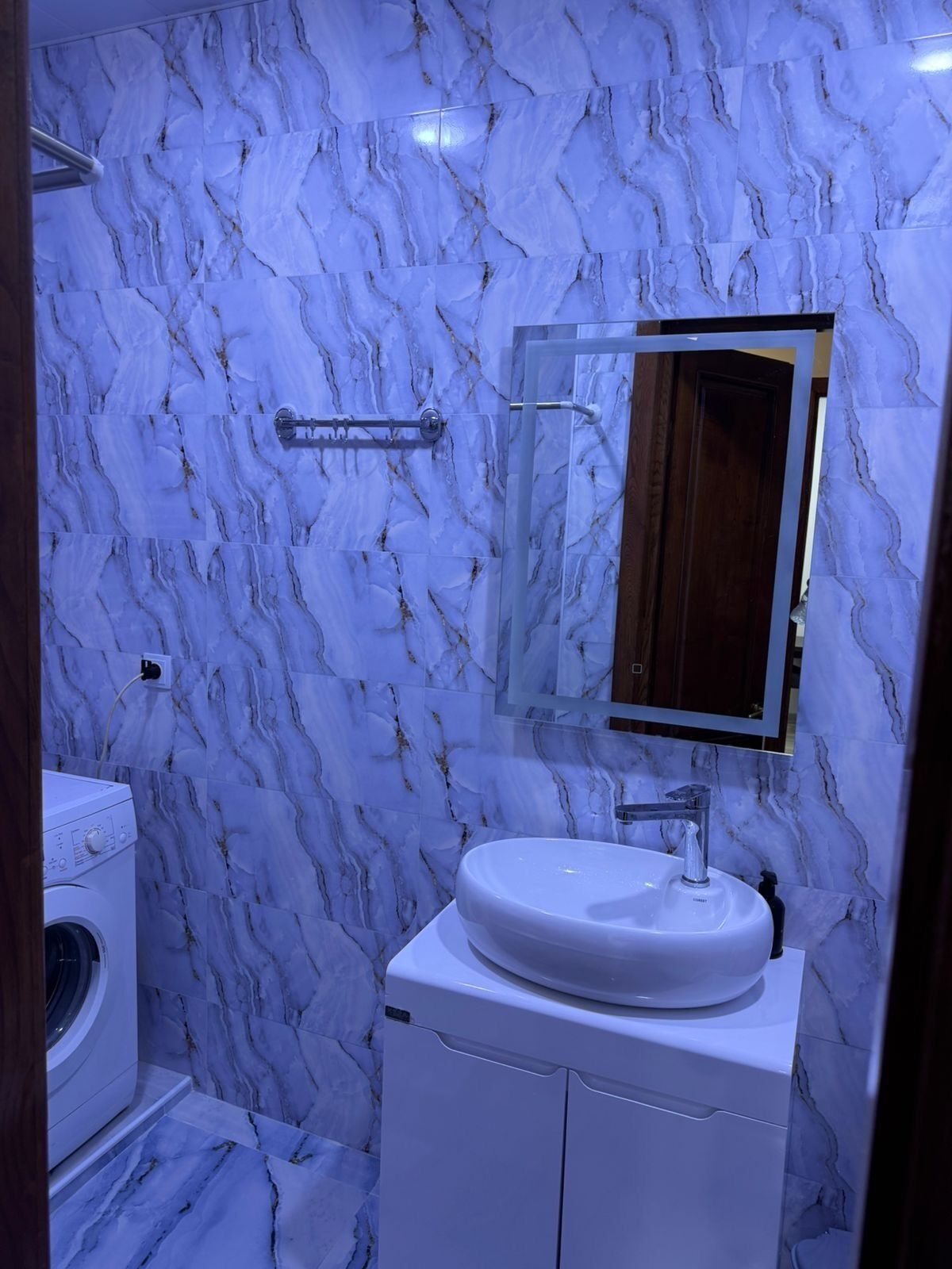 A bathroom with a marble wall, a sink, a mirror, and a washing machine.