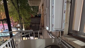 Uma varanda com mesa, duas cadeiras, guarda-corpo e vista para a rua.