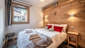 Ein Schlafzimmer mit Holz-Kopfteil, einem Bett mit weißer Bettwäsche und roten Kissen, einem Nachttisch und einem Fenster mit Vorhängen.