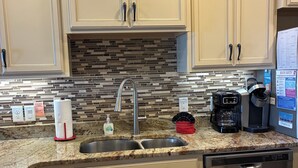 A kitchen with beige cabinets, a granite countertop, a stainless steel dishwasher, and a coffee maker. - Beach Front Townhome – 2 BR, 3 BA - Deck Overlooking Gulf & Steps to the Beach (Panama City Beach)