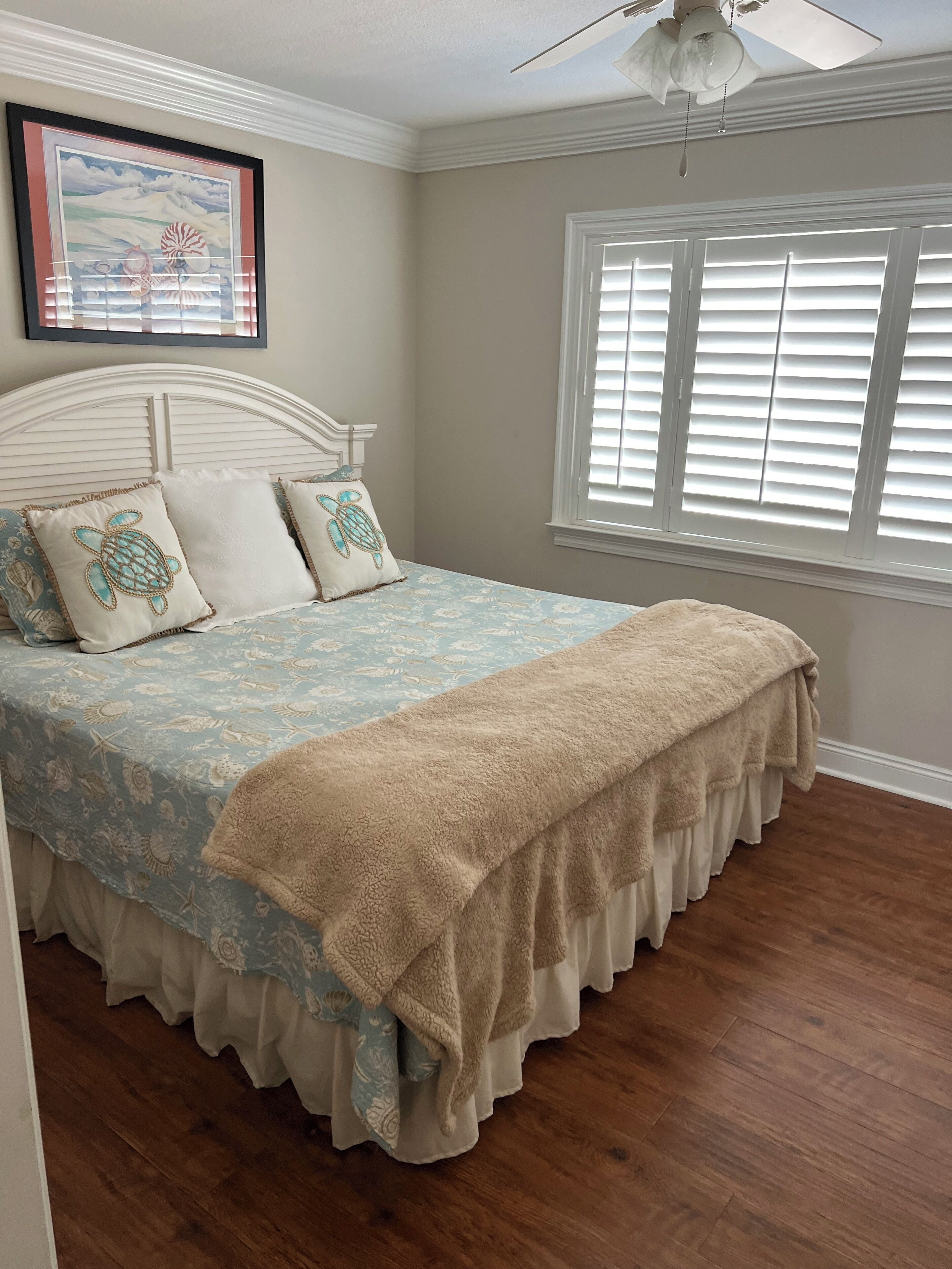 A bedroom with a bed, a ceiling fan, a window with blinds, and a framed picture on the wall.