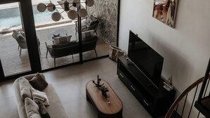 A modern living room with a large window overlooking a beach, a sofa, a TV, and a wooden staircase.