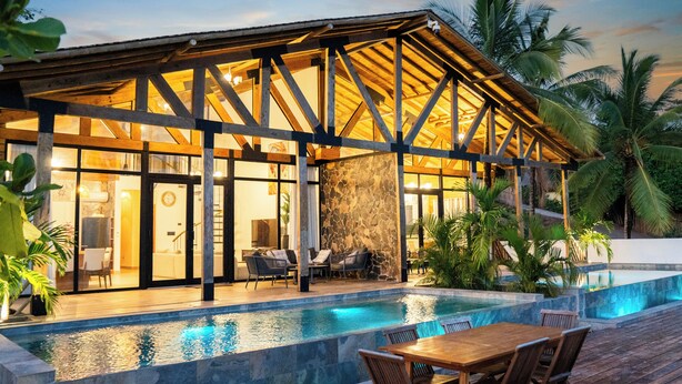 A modern villa with a pool, wooden deck, and stone walls.