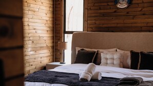 A neatly made bed with a rolled towel, a dark throw blanket, and several pillows.