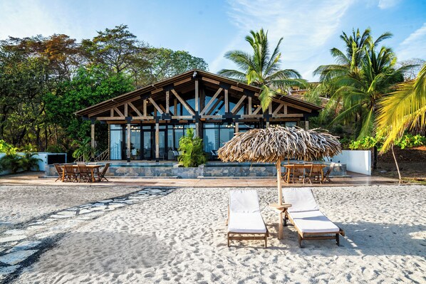 A beachside resort with a wooden structure, lounge chairs, and a thatched umbrella.