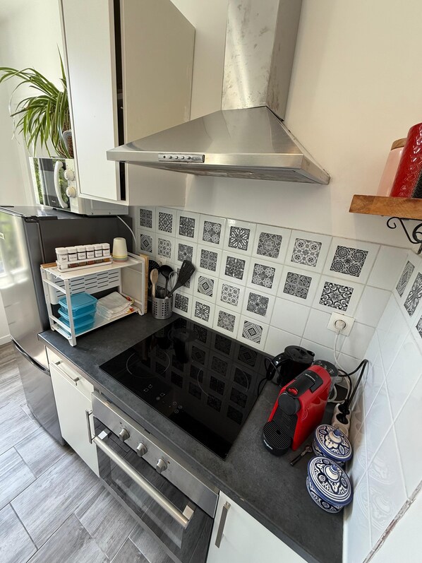 A modern kitchen with a black stovetop, stainless steel range hood, and patterned backsplash tiles.