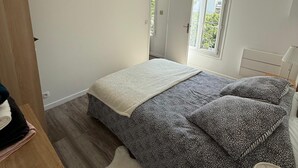 Une chambre à coucher avec un lit, une armoire en bois, une lampe suspendue et une fenêtre donnant sur l’extérieur.
