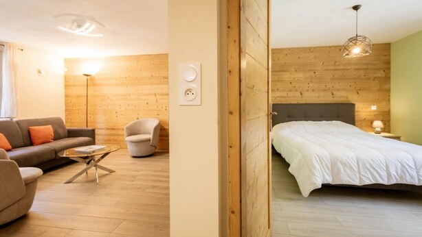 A modern room with a wooden floor, a bed with white bedding, a grey sofa, a small round table, and a chair. - 350m from ski lifts, 1st floor, parking, 67m², Valloire (Valloire)