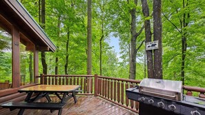 A wooden deck with a grill and picnic table, surrounded by trees.