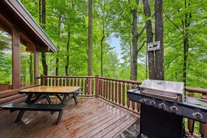 A wooden deck with a grill and picnic table, surrounded by trees.