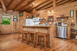 A wooden cabin interior with a kitchen area featuring a refrigerator, microwave, and bar stools. - Resort Amenities and Game Room Fun Await! (Sevierville)