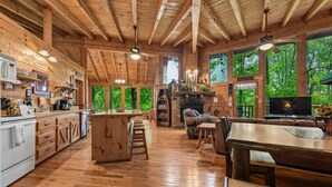 A spacious wooden cabin interior with a kitchen, dining area, and fireplace.