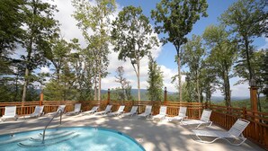 A pool area with lounge chairs and a wooden deck overlooking a mountainous landscape.
