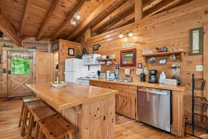Eine Küchenzeile im Holzbau mit Kochinsel, Barhocker, Kühlschrank und einer Kaffeestation.