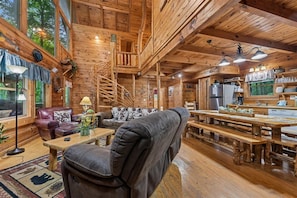 A wooden cabin interior with a dining area, a sofa, a fireplace, and a spiral staircase.