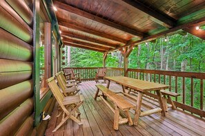 A wooden deck with picnic tables and chairs, surrounded by a wooden railing, overlooking a forested area. - Spacious Cabin w/ Pool Table, Hot Tub & Views (Sevierville)