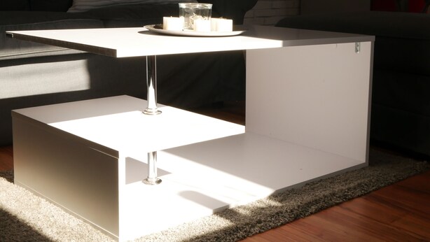 A white, minimalist table with a glass top and candles, placed on a rug in a living room with a black sofa and a white brick wall in the background. - Sunny apartment, 2 rooms (Looft)
