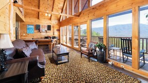 A wooden cabin interior with a living area, dining space, and large windows offering mountain views. - Memorable Mountain Views w/ Hot Tub (Sevierville)