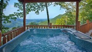 Ein Whirlpool mit Holzterrasse und Geländer, umgeben von üppiger Vegetation und einer Bergkulisse.
