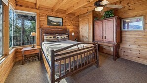 Ein Schlafzimmer einer Holzhütte mit einem Bett, einem Nachttisch, einem Schrank und einem Deckenventilator.
