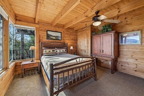 A wooden cabin bedroom with a bed, a nightstand, a cabinet, and a ceiling fan.