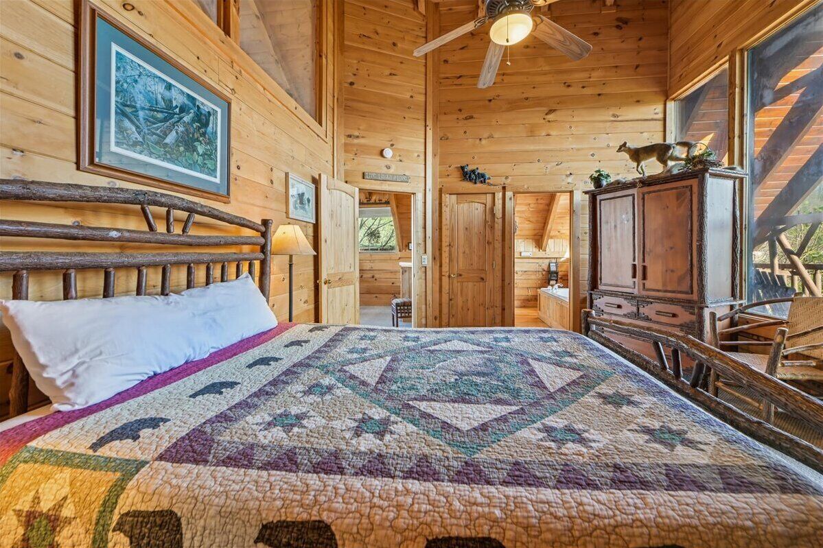 Interior de una cabaña de madera con una cama, un ventilador de techo, un cuadro enmarcado y un aparador de madera.