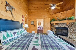 Ein Holzblockhaus-Innenraum mit einem Bett, einem Kamin und einem Deckenventilator.
