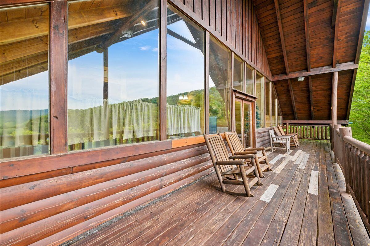 A wooden deck with a view of a mountain landscape, a covered area with large windows, and a wooden bench.