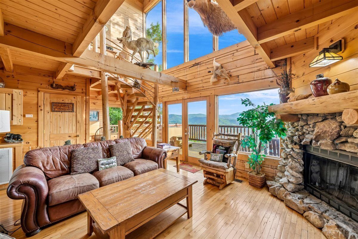Un interior de madera con un sofá de cuero, una chimenea de piedra y vistas amplias a través de grandes ventanales.