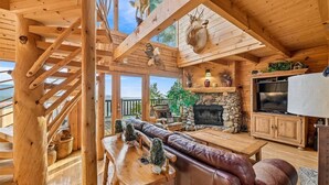 A wooden cabin interior with a stone fireplace, leather seating, and a television.