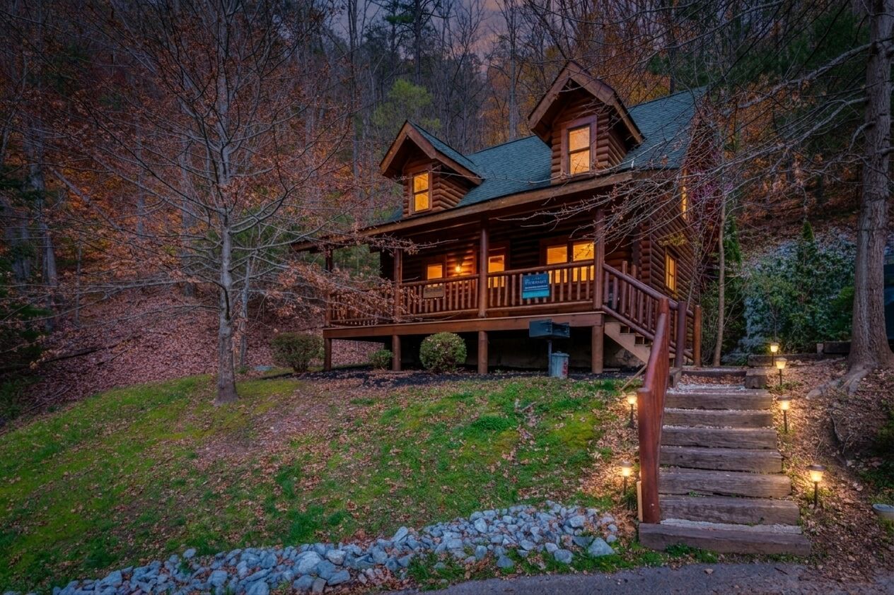 Un chalet rustique doté d’un porche, entouré d’arbres et accessible par un sentier de pierres menant à l’entrée.