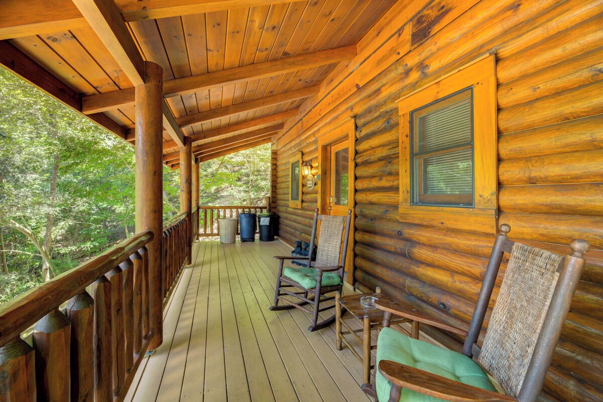 A wooden cabin with a porch, rocking chairs, and a view of the forest.