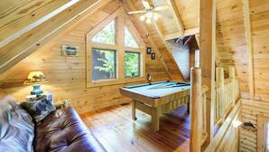Acogedor cuarto ático con mesa de billar, paredes de madera y ventanas grandes.