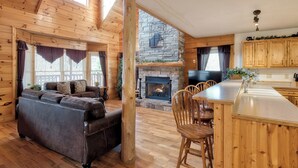 A log cabin interior with a fireplace, wooden furniture, and a stone wall. - Mountain Escape w/ Game Room, Hot Tub & Views (Sevierville)