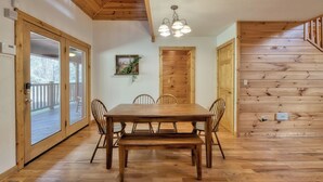 A wooden dining table with chairs, a bench, and a chandelier in a room with wooden walls and a wooden staircase. - Mountain Escape w/ Game Room, Hot Tub & Views (Sevierville)