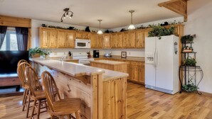 A kitchen with wooden cabinets, a central island with chairs, a refrigerator, and pendant lights. - Mountain Escape w/ Game Room, Hot Tub & Views (Sevierville)