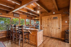 L’intérieur d’un chalet en bois comprend un coin cuisine, des tabourets de bar et une grande porte en bois portant l’inscription « MINDRY ».