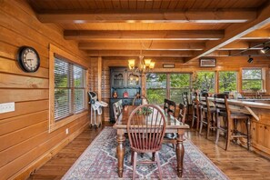 A wooden interior with a dining table, chairs, a chandelier, and a clock on the wall.