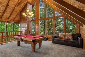 Un intérieur en bois avec une table de billard, un canapé et de grandes fenêtres.