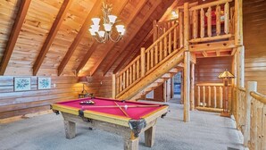 Un intérieur en bois avec une table de billard, un escalier et un lustre.