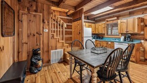 Ein Holzblockhaus-Innenraum mit Esstisch, Stühlen, einer Küchenzeile und einer Bärenstatue.