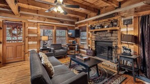 Ein Blockhaus-Interieur mit Kamin, Holzwänden, Deckenventilator und einer Couch.