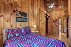 Una habitación con paneles de madera, una cama y un ventilador de techo, con un cartel que dice 'END OF THE RAINBOW'.