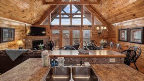 A log cabin interior with a kitchen island, dining area, fireplace, and large windows. - Spacious Lodge w/ Scenic Views & Resort Amenities (Gatlinburg)