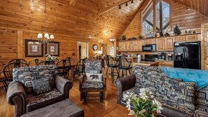 A log cabin interior with a dining area, kitchen, and seating with patterned cushions. - Spacious Lodge w/ Scenic Views & Resort Amenities (Gatlinburg)