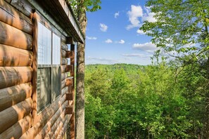 A log cabin with a window overlooking a forested landscape.