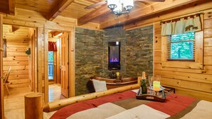 Een gezellige blokhutkamer met een stenen openhaard, een bed met een rood-witte deken en een raam met gordijnen.